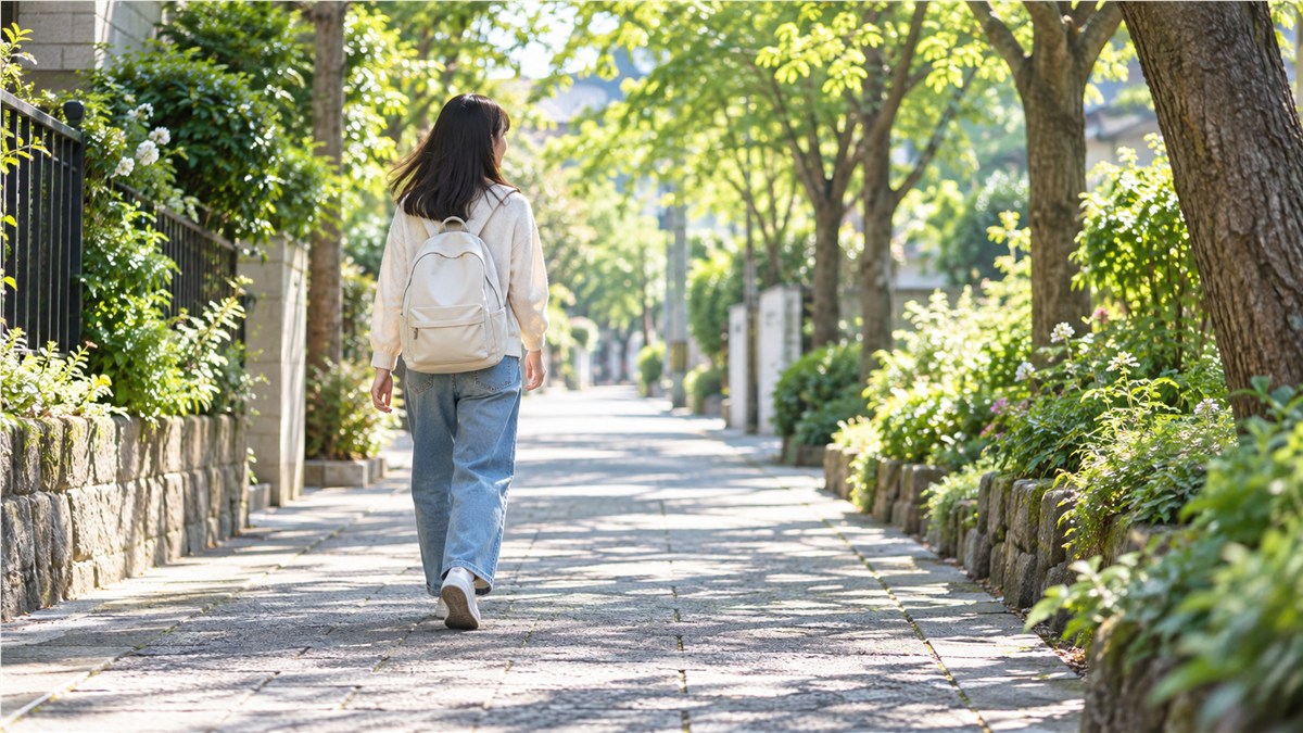 朝の木漏れ日が差す並木道を、私服でリュックを背負って歩く日本人の10代の子どもの後ろ姿