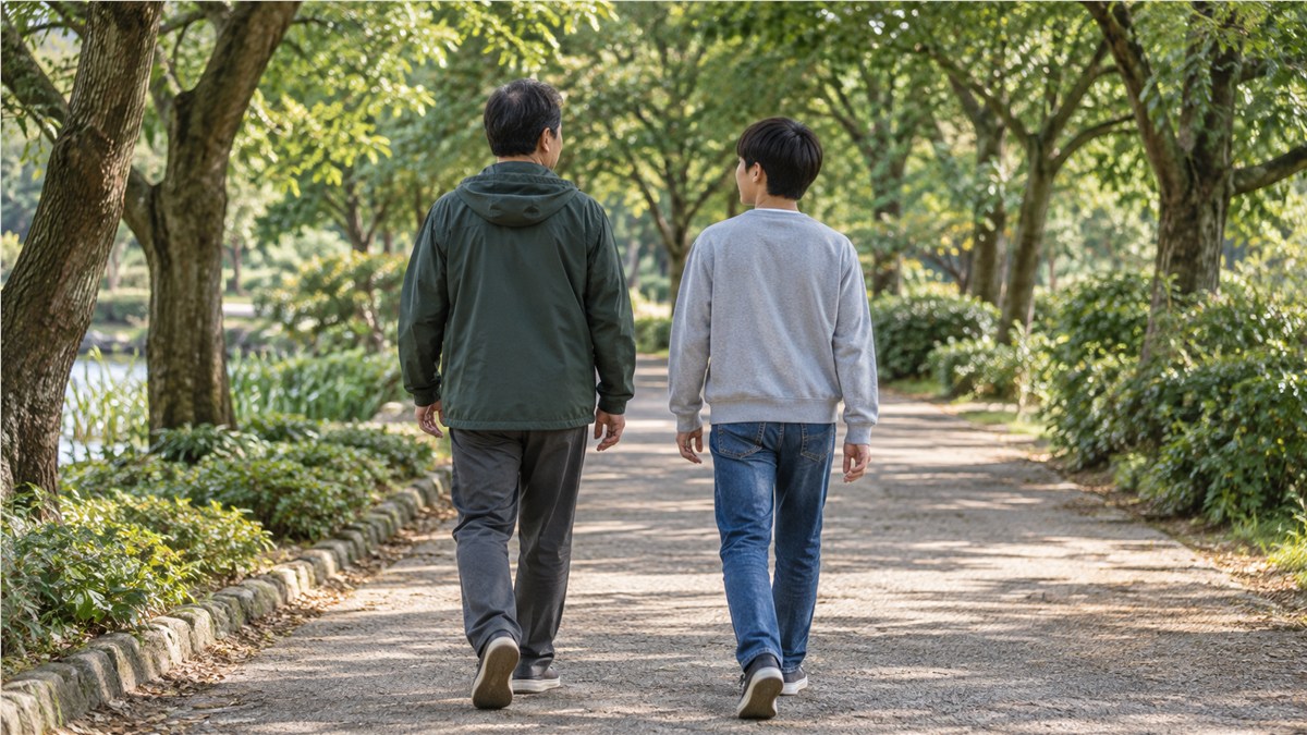 午後のやわらかな光の公園の並木道を、私服の日本人の父親と中学生の息子が並んで歩く後ろ姿